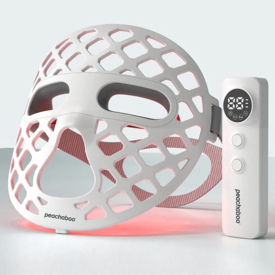 A white silicone mask glowing with red light, showcasing the Peachaboo Glo Aurora LED light therapy technology.

