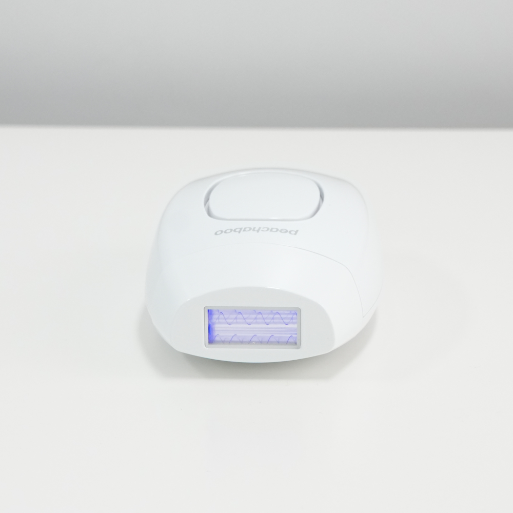 A sleek white electronic hair remover, the Peachaboo Laser IPL, displayed on a table for easy access and convenience.